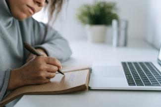 woman writing goals in a notebook with a laptop nearby