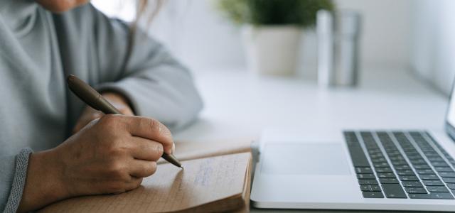 woman writing goals in a notebook with a laptop nearby